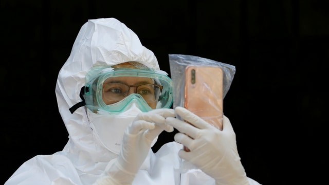 Seorang pekerja medis yang mengenakan pakaian pelindung menggunakan telepon genggam yang dibungkus dengan plastik. Foto: REUTERS / Willy Kurniawan