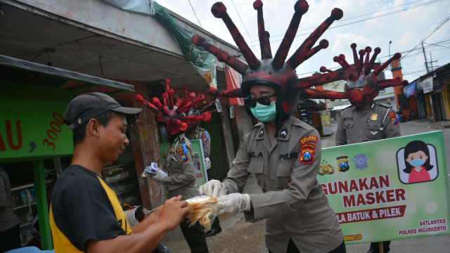 Anggota polisi lalu lintas Polres Mojokerto membagikan masker dengan memakai helm virus corona di pasar tradisional Sawahan, Jawa Timur. Foto: ANTARA FOFO/Syaiful Arif
