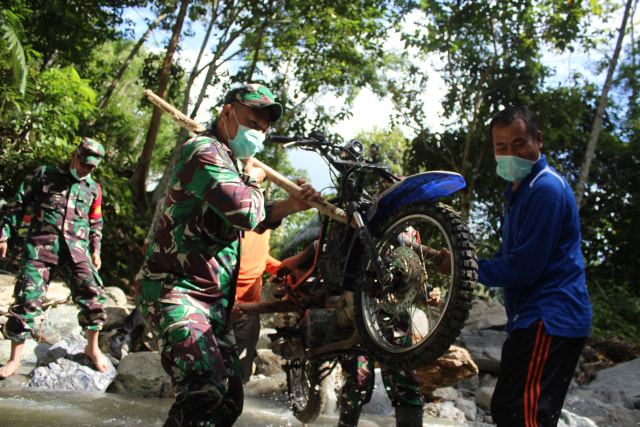 TNI dan masyarakat setempat memikul motor menuju sasaran TMMD. Foto: Lukman Budianto/Kendarinesia