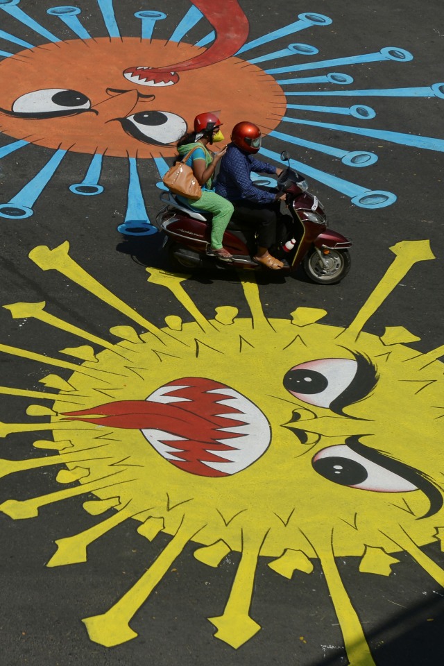 Pengedara motor melintasi grafiti virus corona di Chennai, India. Foto: AFP/Arun SANKAR