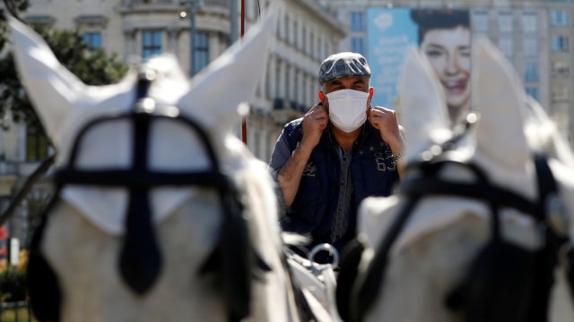 Seorang kusir menggunakan masker dengan kereta kuda Fiaker menunggu paket makanan untuk pengiriman di depan Hotel InterContinental, Wina, Austria. Foto: REUTERS / Leonhard Foeger