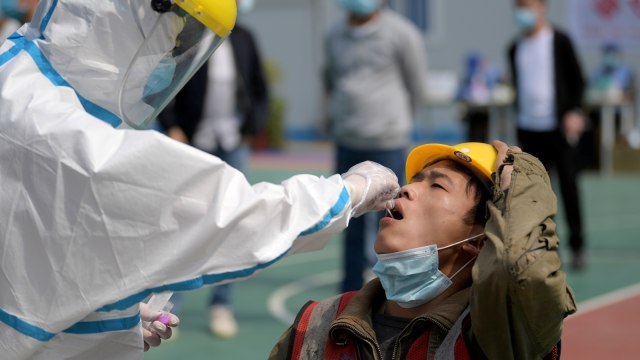 Seorang pekerja medis yang memakai pakaian pelindung melakukan uji asam nukleat kepada seorang pekerja di Wuhan, Provinsi Hubei, China. Foto: China Daily via REUTERS