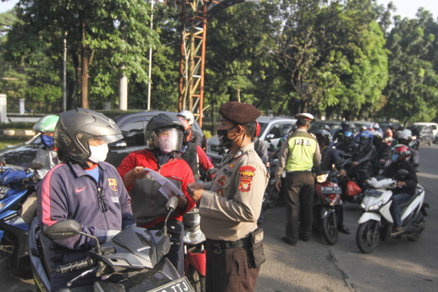 Petugas kepolisian memeriksa identitas pengendara motor yang berpenumpang saat penerapan PSBB di Perbatasan Jakarta - Depok, Depok, Jawa Barat, Rabu (15/4). Foto: ANTARA FOTO/Asprilla Dwi Adha