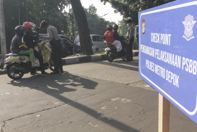 Petugas kepolisian memeriksa identitas pengendara motor yang berpenumpang saat penerapan PSBB di Perbatasan Jakarta - Depok, Depok, Jawa Barat, Rabu (15/4).  Foto: ANTARA FOTO/Asprilla Dwi Adha