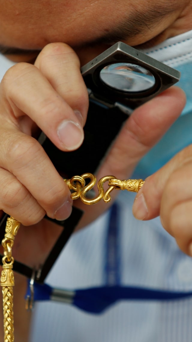Seorang penjaga toko emas di Bangkok, Thailand memeriksa kondisi perhiasan yang akan dijual. Foto: REUTERS/Jorge Silva