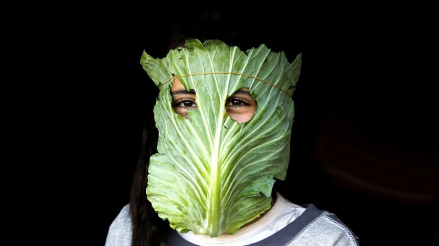 Seorang anak memakai topeng yang terbuat dari kubis saat ibunya sedang memasak di Beit Lahia, Jaluar Gaza, Palestina. Foto: AFP/MOHAMMED ABED