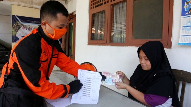 Petugas PT Pos Indonesia menyerahkan bantuan sosial tunai tahap pertama kepada salah seorang warga di Kota Bogor, Jawa Barat. Foto: Dok. Kemensos