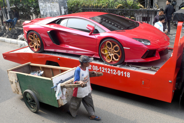 Seorang pria menarik gerobaknya melewati mobil Ferrari yang dikirim ke pemilik di Jakarta. Foto: AFP/Goh Chai Hin