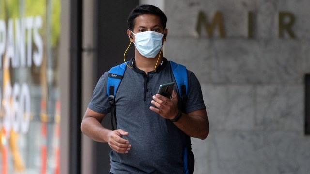 Seorang pria menggunakan masker saat berjalan melewati kawasan pusat bisnis (CBD) di Wellington, Selandia Baru. Foto: Marty MELVILLE / AFP