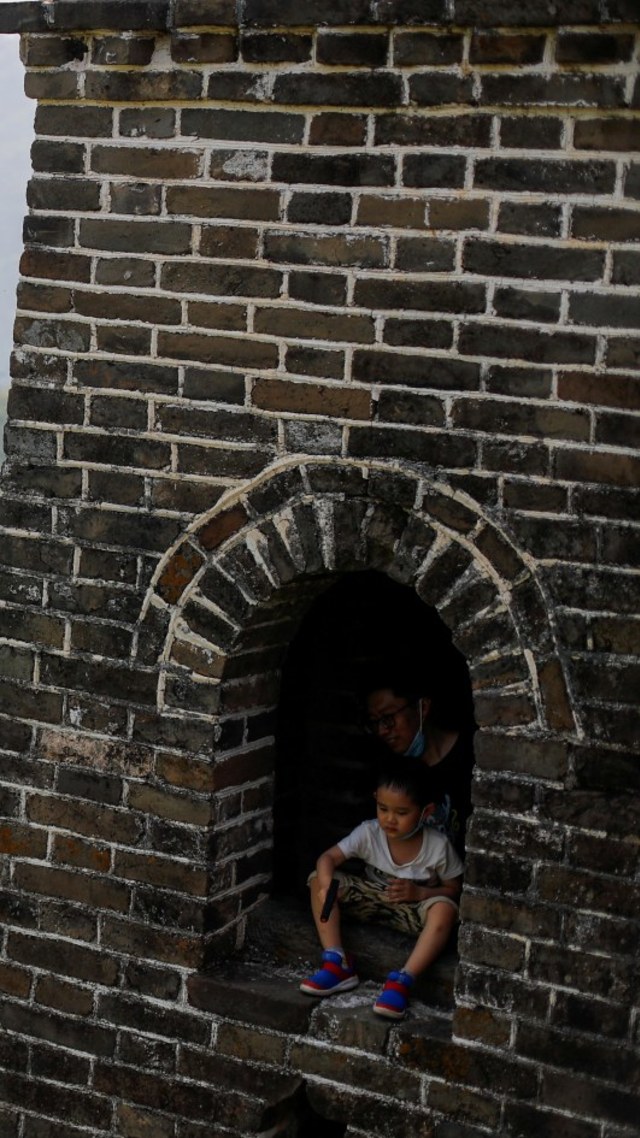 Seorang anak laki-laki duduk di jendela sebuah menara pengawas saat mengunjungi Tembok Besar China, Beijing, Jumat (1/5). Foto: REUTERS / Thomas Peter