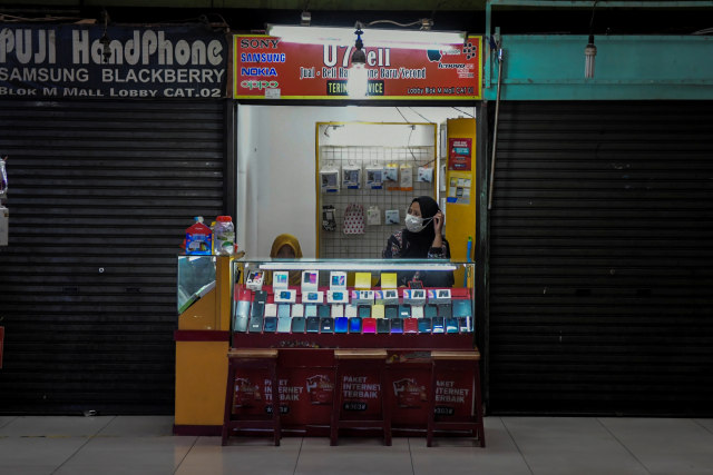 Karyawan menunggu konsumen di sebuah kios telepon seluler yang masih buka di antara kios yang tutup saat merebaknya wabah corona di Terminal Blok M, Jakarta. Foto: ANTARA FOTO/Galih Pradipta
