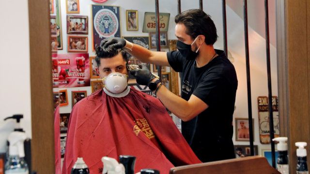Seorang penata rambut mengenakan masker sarung tangan saat memotong rambut pelanggannya di Thessaloniki, Yunani, Senin (4/5). Foto: REUTERS/Murad Sezer