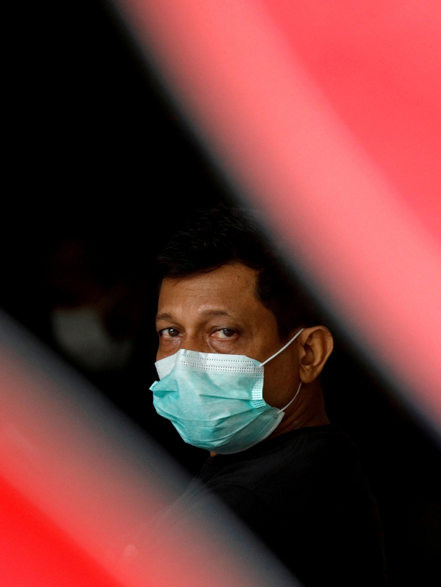 Seorang migran mengenakkan masker menunggu dibawa ke fasilitas medis di Singapura. Foto:  REUTERS / Edgar Su