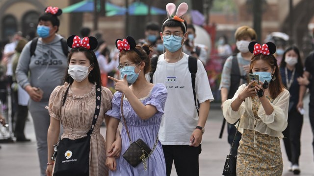 Warga mengenakan masker saat mengunjungi taman hiburan Disneyland di Shanghai, Senin (11/5). Foto: Hector RETAMAL / AFP