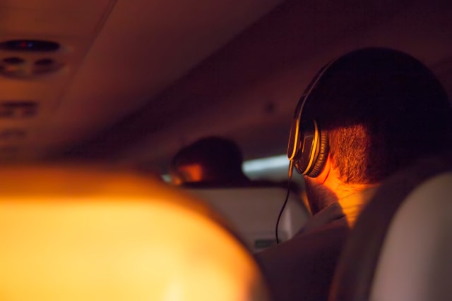 Ilustrasi penumpang pesawat mendengarkan musik saat terbang. Foto: Shutterstock
