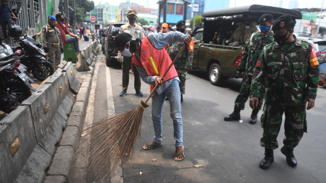 Seorang warga yang terjaring razia penindakan pelanggaran aturan PSBB oleh Satpol PP menjalani hukuman dengan cara membersihkan sampah di Tanah Abang, Jakarta. Foto: ANTARA FOTO/Akbar Nugroho Gumay