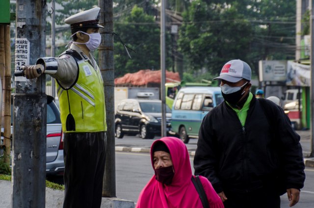 Warga melintas di samping sebuah patung polisi lalu lintas yang dipasangkan masker di Bandung, Jawa barat, Jumat (15/5). Foto: ANTARA FOTO/Novrian Arbi