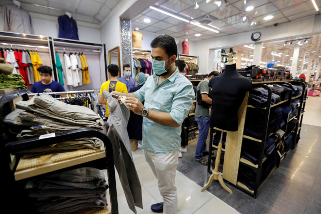 Seorang pria Irak dengan menggunakan masker memilih pakaian di sebuah toko untuk persiapan Idul Fitri. Foto: REUTERS/Thaier al-Sudani