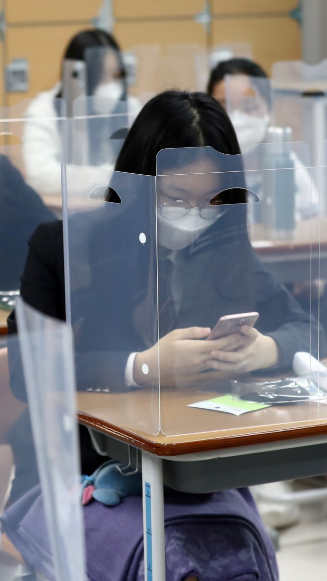 Sejumlah pelajar SMA di Korsel kembali masuk sekolah dengan pembatas plastik di meja belajar, Rabu (20/5). Foto: Yonhap via Reuters