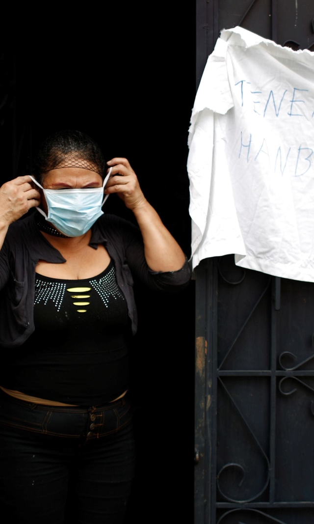 Seorang wanita menggunakan masker di sebelah kain putih bertuliskan "Kami lapar" di San Salvador, El Salvador. Foto: REUTERS/Jose Cabezas