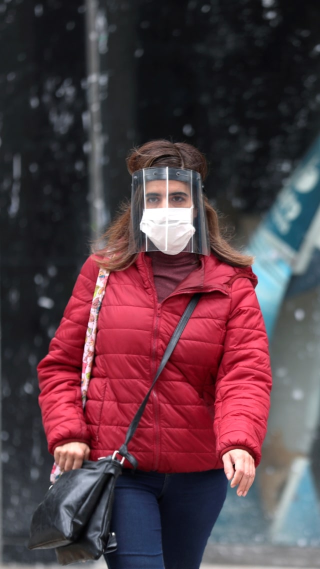 Seorang pria menggunakan masker dan pelindung wajah saat melewati salah satu tempat penukaran uang di pusat kota Buenos Aires, Argentina. Foto: REUTERS/Agustin Marcarian