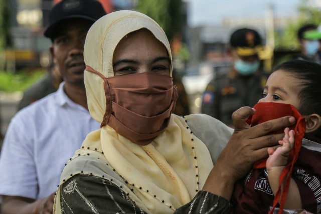Seorang warga memakaikan masker kepada anaknya saat razia di depan Masjid Raya Banda Aceh. Foto: Abdul Hadi/acehkini