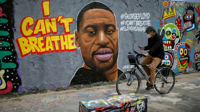 Pengendara sepeda melintasi mural dengan gambar wajah George Floyd di Taman Mauer, Berlin, Jerman. Foto: Odd ANDERSEN / AFP