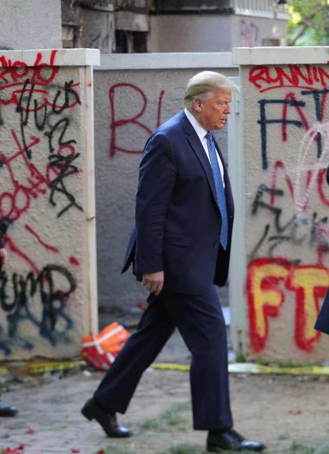 Presiden AS Donald Trump berjalan melewati sebuah bangunan yang dipenuhi coretan grafiti oleh demonstran di Lafayette Park, Washington, Amerika Serikat. Foto: REUTERS / Tom Brenner