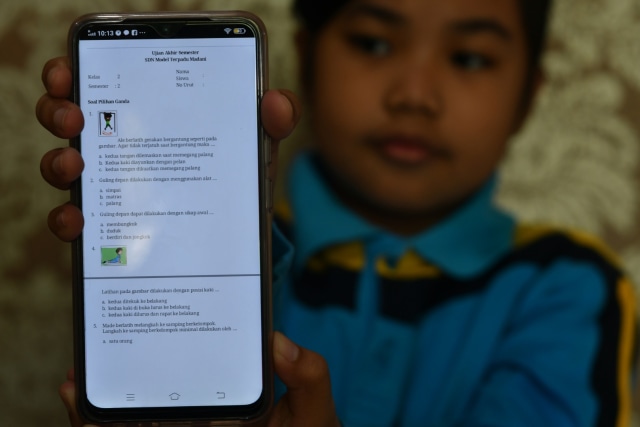 Seorang siswi SDN Model Terpadu Madani menunjukan soal ujian akhir semester (UAS) yang dikerjakan secara daring di rumahnya di Palu, Sulawesi Tengah, (4/6). Foto: ANTARA FOTO/Mohamad Hamzah