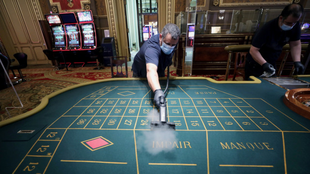 Karyawan menggunakan masker membersihkan mesin slot sebelum pembukaan kembali Monte Carlo Casino di Monako. Foto: REUTERS / Eric Gaillard