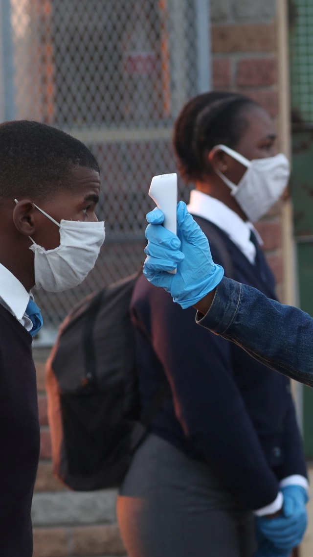 Seorang guru memeriksa suhu siswa sebelum masuk sekolah untuk pertama kali setelah lockdown akibat virus corona di Cape Town, Senin (8/6). Foto: Reuters/Mike Hutchings