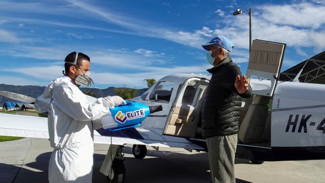 Petugas menyemprotkan cairan disinfektan kepada penumpang pesawat pribadi yang membantu menangani wabah COVID-19 di Kolombia. Foto: Reuters/LUIS JAIME ACOSTA; 