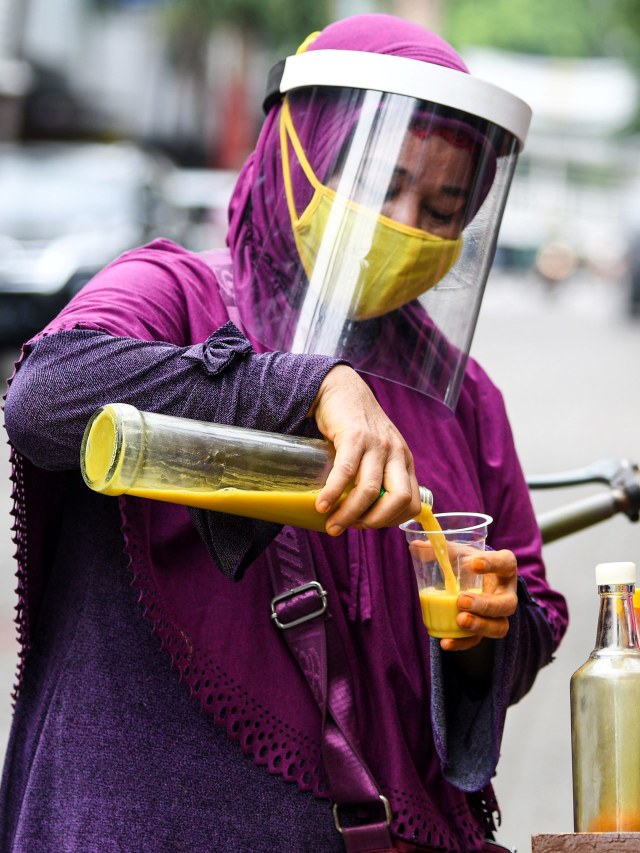 Penjual jamu keliling gunakan masker dan pelindung wajah saat berjualan di kawasan Pasar Baru, Jakarta Pusat. Foto: ANTARA FOTO/M Risyal Hidayat