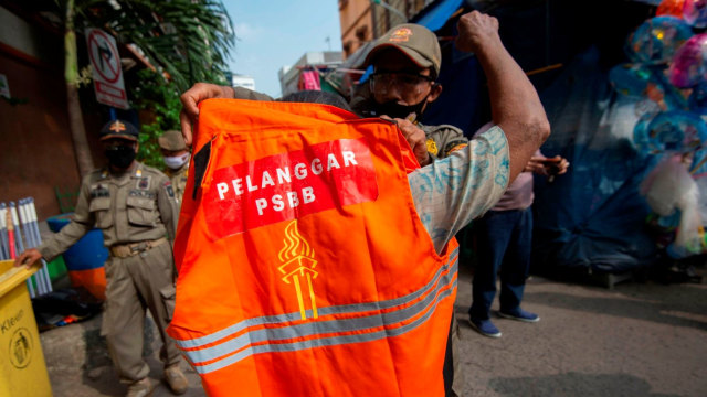Petugas Satpol PP mengenakan rompi khusus kepada pelanggar aturan pembatasan sosial berskala besar (PSBB) di Pasar Jatinegara, Jakarta. Foto: ANTARA FOTO/Aditya Pradana Putra