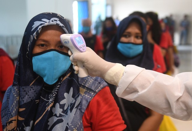 Sorang TKI Ilegal yang dipulangkan dari Malaysia melakukan pemeriksaan suhu tubuh di Pelabuhan Tanjung Priok, Jakarta, Jumat (12/6). Foto: Akbar Nugroho Gumay/ANTARA FOTO