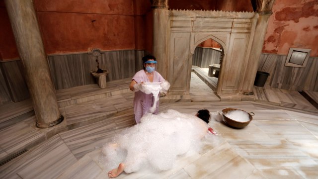 Pemijat menggunakan pelindung wajah saat memandikan dan memijat pelanggan Cemberlitas Hammam di Istanbul, Turki. Foto: Murad Sezer/Reuters