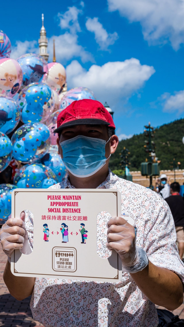 Seorang pekerja memegang tanda yang mengingatkan pengunjung untuk menerapkan jaga jarak di Disneyland Hong Kong, Kamis (18/6). Foto: Anthony WALLACE/AFP
