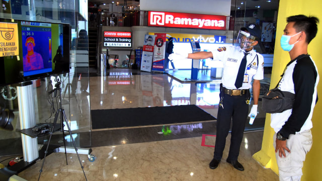 Petugas keamanan memeriksa suhu tubuh pengunjung melalui layar saat pembukaan kembali pusat perbelanjaan Mall BTM, Kota Bogor, Jawa Barat. Foto: ANTARA FOTO/Arif Firmansyah