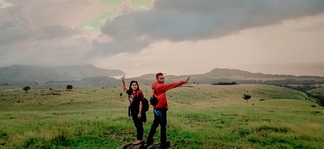 Pengunjung berfoto dengan latar padang hijau di Bukit Nangarasong. Foto: Riky Saba.