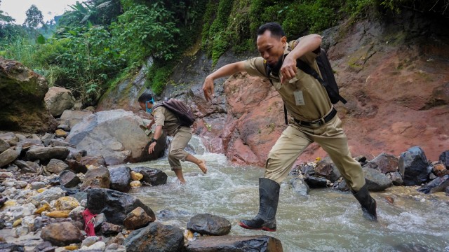 Kepala Sekolah SMP N 4 Bawang Mulud Sugito (kanan) dan guru Wiyata Bhakti melewati aliran sungai di dasar bukit saat mengantar lembar tugas siswa. Foto: Aditya Pradana Putra/Antara Foto