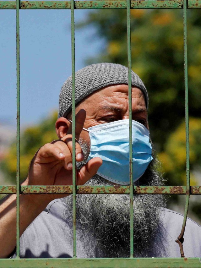 Salah seorang pelayat mengenakan masker saat menyaksikan memakamkan seorang wanita yang terkena virus corona. Foto: Mussa Qawasma/REUTERS