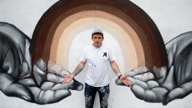 Nathan Murdoch seniman mural asal Inggris berpose pada karyanya yang mengangkat tema Anti Rasisme. Foto: Andrew Couldridge/REUTERS