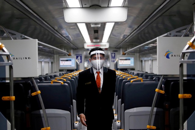Seorang karyawan yang mengenakan  pelindung wajah dan masker berjalan di dalam kereta Railink. Foto: Willy Kurniawan/REUTERS