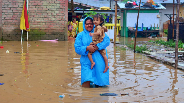 Seorang ibu menggendong anaknya melintasi genangan lumpur sisa banjir. Minggu, (5/7). Foto: Dok banthayoid (Wawan Akuba)