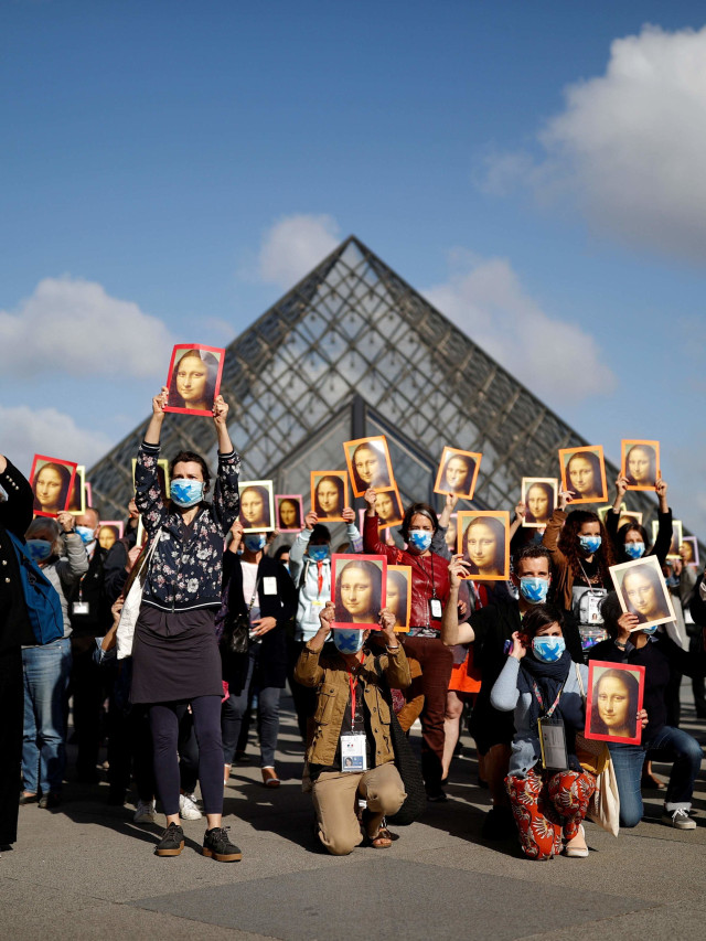 Aksi damai pemandu wisata Paris sambil memegang poster Mona Lisa di halaman museum Le Louvre. Foto: Christian Hartmann/REUTERS