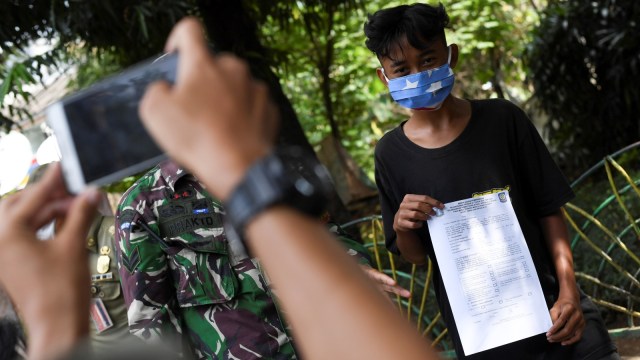Petugas mengambil foto seorang warga dengan membawa surat bukti pelanggaran karena tidak mengenakan masker di Jakarta, Selasa (7/7). Foto: Wahyu Putro A/Antara Foto