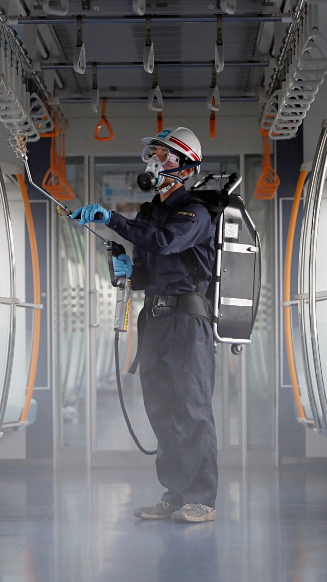 Pekerja yang mengenakan masker dan kacamata pelindung menyemprotkan bahan kimia pada kursi untuk penumpang, Kamis (9/7). Foto: Issei Kato/Reuters