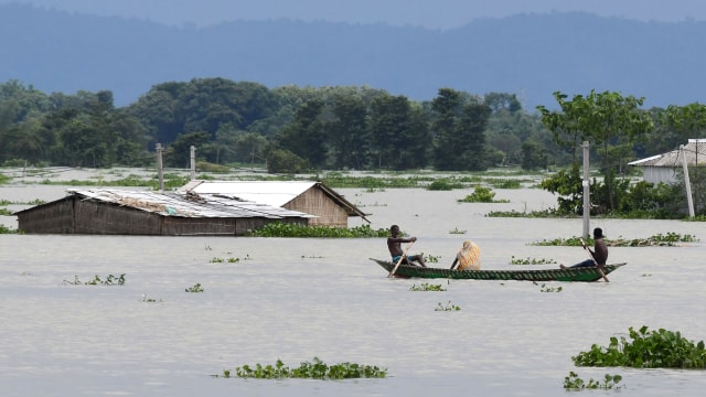 Penduduk desa mendayung perahu di dekat rumah yang terendam banjir di Assam di India. Foto: Biju BORO / AFP