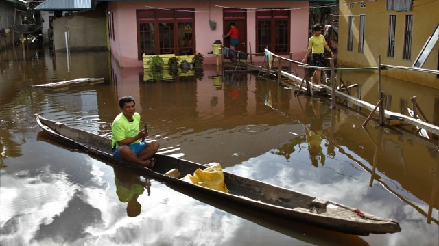 Warga melintas dengan menggunakan perahu di dekat rumahnya yang terendam banjir di Desa Rumbia, Kecamatan Bondoala, Konawe, Sulawesi Tenggara, Jumat (17/7/2020). Foto: Jojon - Antara Foto