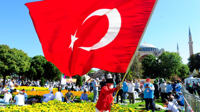 Seorang pria mengibarkan bendera Turki di luar Hagia Sophia, di Istanbul, Turki, Jumat (24/7). Foto: Omer Kuscu/AP Photo
